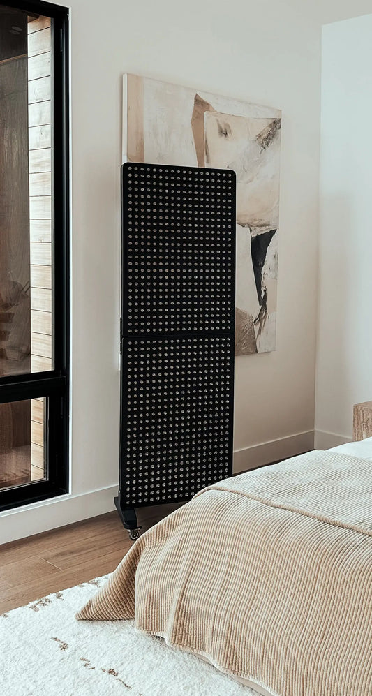 light therapy panel standing in a modern bedroom next to a window with art on the wall